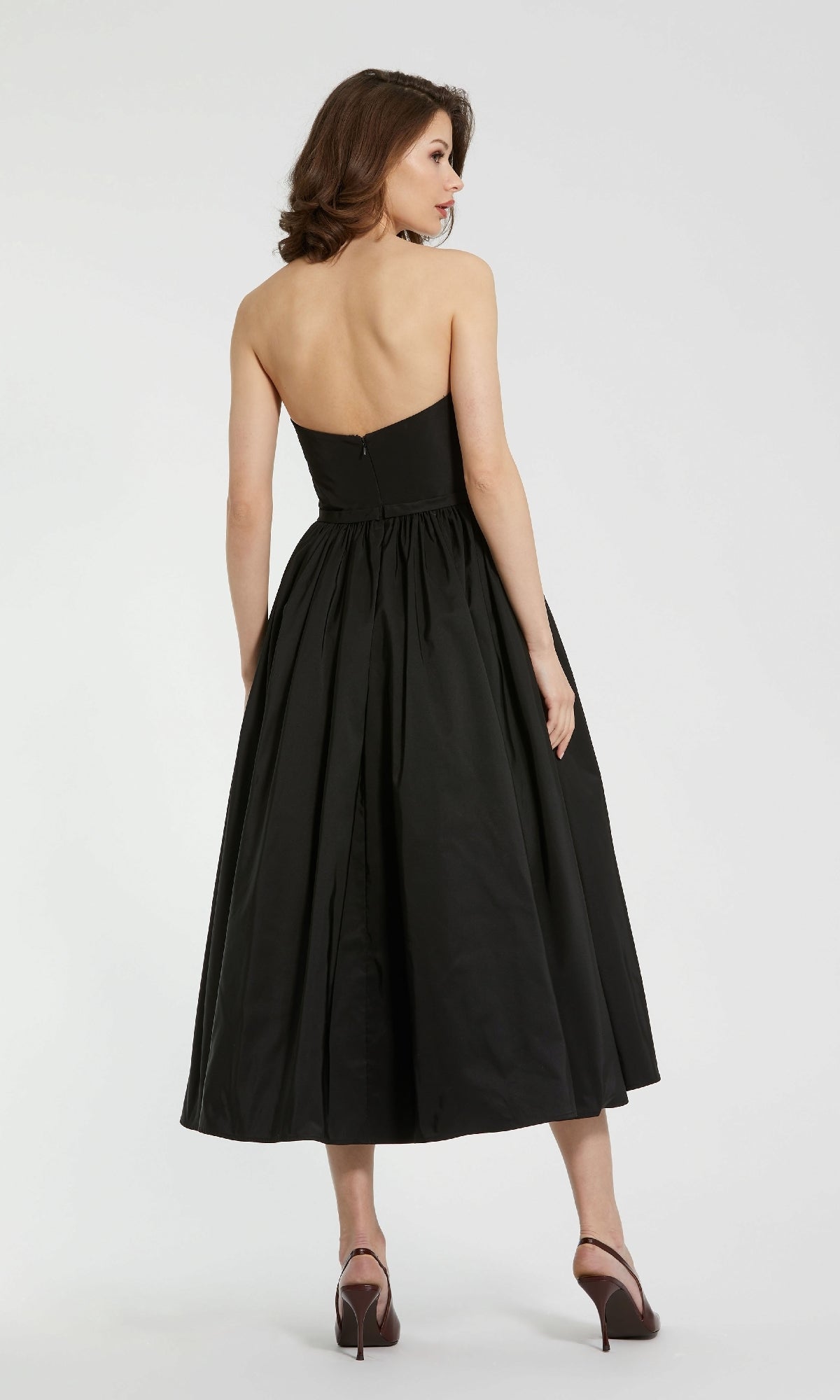 A woman in the Mac Duggal 21023 midi strapless semi-formal dress and high heels stands with her back to the camera against a plain background.